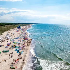 Słoneczna plaża w Darłowie tętni życiem. Tłumy plażowiczów, kolorowe parawany i namioty, a w wodzie kąpielowicze i surferzy. To idealne miejsce na wakacyjne atrakcje.