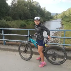 Kobieta na rowerze na moście, gotowa do odkrywania malowniczych velo tras rowerowych wzdłuż rzeki.