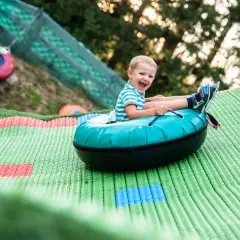 Uśmiechnięty chłopiec zjeżdża na pontonie po zielonej zjeżdżalni w Oponkowej Krainie w Szklarskiej Porębie.