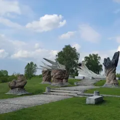Pomnik w Białymstoku, jedna z jego atrakcji, z kamiennymi rzeźbami i betonowymi formami na tle zieleni i błękitnego nieba.