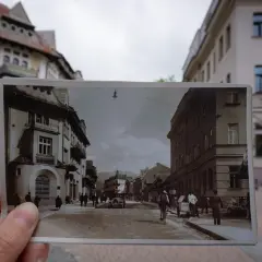 Dawne zakopane atrakcje na pocztówce: ulica z kamienicami, ludźmi i wozami. W tle współczesne budynki.