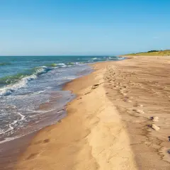 Piękne, dzikie plaże nad Bałtykiem. Fale delikatnie obmywają piaszczysty brzeg, a na piasku widać ślady stóp.