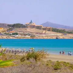 Costa Calma atrakcje: piaszczysta plaża, turkusowe morze, hotel na wzgórzu i windsurfer.