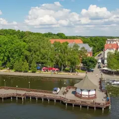Drewniane molo z altaną i łodziami, nad jeziorem w otoczeniu zieleni i urokliwego miasteczka. Idealne mazury atrakcje dla każdego.