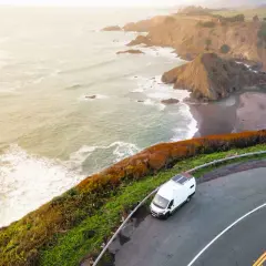 Biały kamper na krętej drodze wzdłuż wybrzeża Pacyfiku, idealny na road trip USA. Fale rozbijają się o skaliste klify.