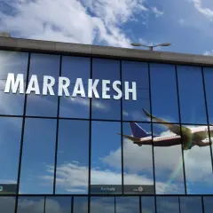 Samolot wznosi się na tle błękitnego nieba z chmurami, odbijając się w szklanej fasadzie lotniska w Marrakeszu.