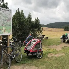 Góry Izerskie rowerem: mapa tras, rowery z przyczepkami i ludzie odpoczywający na ławce.