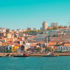 Widok na kolorowe kamienice i nowoczesne budynki Porto, idealne na weekendowy wypad. Rzeka Douro i łodzie dodają uroku.