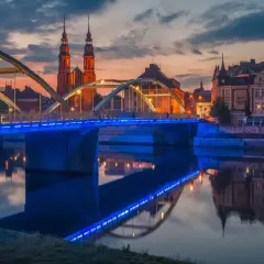 Zachód słońca nad Odrą, most z niebieskim podświetleniem i katedra w tle. Odkryj magiczne miejsca opolskie.