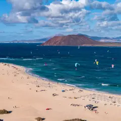 Fuerteventura, gdzie najlepiej? Plaża z kitesurferami i turystami, w tle wulkan i góry. Idealne miejsce na wakacje.