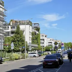 Nowoczesne osiedle w jednej z dzielnic Warszawy. Długi blok mieszkalny z balkonami, drzewa i zaparkowane samochody.