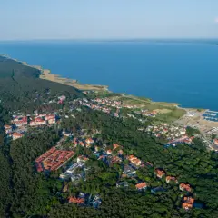 Widok z lotu ptaka na Krynicę Morską. Widoczne plaże, lasy, zabudowania i port. Mnóstwo atrakcji czeka na turystów.