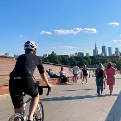 Rowerzysta na trasie rowerowej wzdłuż Wisły w Warszawie, z widokiem na panoramę miasta.