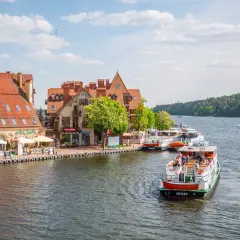 Port w Giżycku z cumującymi statkami i budynkami z czerwonymi dachami. Widać łodzie wycieczkowe, idealne na odkrywanie giżyckich atrakcji.