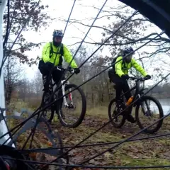 Dwóch rowerzystów w jaskrawożółtych kurtkach przemierza leśny bursztynowy szlak rowerowy.