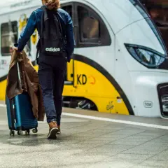 Podróż pociągiem nad morze. Mężczyzna z walizką i kurtką idzie na peronie w stronę nowoczesnego pociągu.