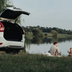 Rodzina cieszy się piknikiem nad jeziorem, planując długie weekendy 2026. Otwarty bagażnik białego SUV-a sugeruje gotowość na przygodę.