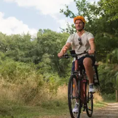 Mężczyzna w kasku jedzie rowerem po leśnej ścieżce, odkrywając malownicze trasy rowerowe Poznań.