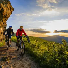 Dwóch rowerzystów przemierza malownicze trasy rowerowe w górach o zachodzie słońca.