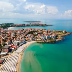 Malownicze wybrzeże Bułgarii nad turkusowym morzem. Miasto z czerwonymi dachami rozciąga się wzdłuż piaszczystej plaży z białymi parasolami.