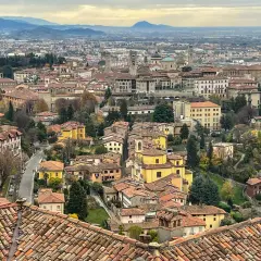 Widok na wzgórza i dachy Bergamo, miasta bliskiego Mediolanowi. W oddali widać góry.