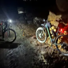 Dwa rowery z włączonymi światłami stoją na wilgotnej ścieżce. Nocna wyprawa po trasach rowerowych Elbląg.