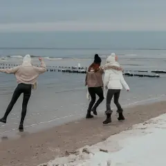 Trzy dziewczyny cieszą się zimą nad morzem, biegając po plaży z resztkami śniegu.