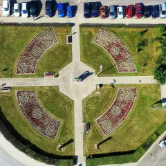 Piątek miasto środek Polski. Park miejski z klombami w kształcie łuków, alejkami i ławkami. W tle parking z samochodami.