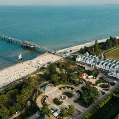 Widok na plażę, molo i białe budynki z dachami w szpic na wyspie Uznam. W oddali widać diabelski młyn.