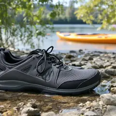 Szare buty sportowe na kamienistej plaży, idealne jako jakie buty na kajaki. W tle żółty kajak na wodzie.