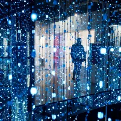Osoba wchodzi do instalacji świetlnej, jednego z nietypowych miejsc w Warszawie. Błękitne światła tworzą iluzję nieskończoności.