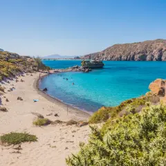 Piękna plaża na wyspie Nisyros z turkusową wodą, łodzią i ludźmi odpoczywającymi na piasku.
