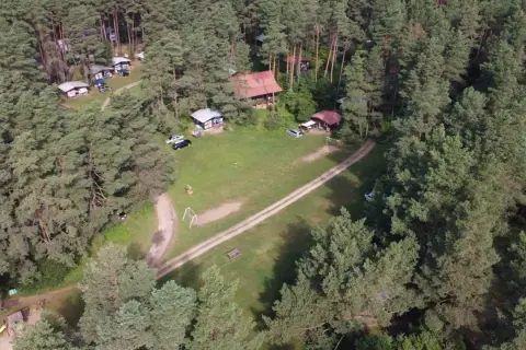 Malowniczy widok na stanicę wodną Zgon otoczoną lasem sosnowym. Widać domki, samochody i plac zabaw.