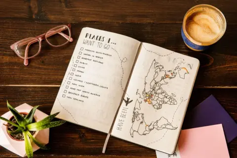 Planowanie wakacji: lista miejsc do odwiedzenia, mapa świata z zaznaczonymi podróżami, okulary i kawa.