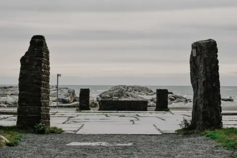 Kamienne filary i kamienna ława na placu przy morzu, jakby na **verdens ende**.