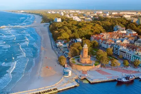 Malownicze polskie wybrzeże miejscowości z latarnią morską, plażą i portem.