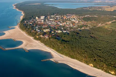 Jarosławiec atrakcje: malownicza plaża z falochronami, las sosnowy i zabudowania kurortu widziane z lotu ptaka.