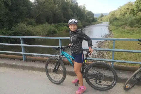 Kobieta na rowerze na moście, gotowa do odkrywania malowniczych velo tras rowerowych wzdłuż rzeki.