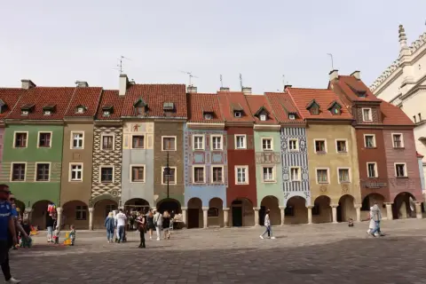 Kolorowe kamieniczki na Starym Rynku w Poznaniu, wspaniałe poznańskie atrakcje. Ludzie spacerują po brukowanym placu.