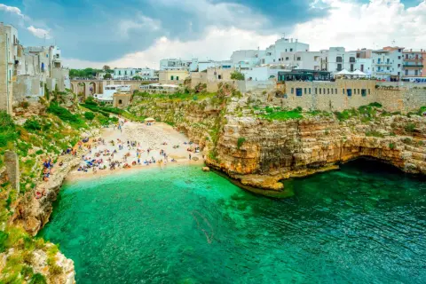 Malownicza plaża Polignano a Mare z turkusową wodą, skalistymi klifami i białymi budynkami na szczycie.