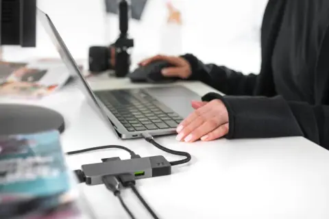 Praca zdalna i turystyka w jednym. Ktoś planuje podróż, przeglądając oferty na laptopie, podłączonym do hubu USB.