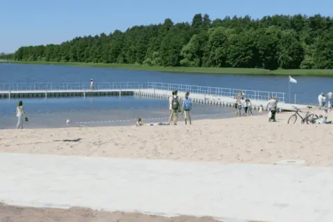 Słoneczne plaże na Mazurach przyciągają ludzi. Dzieci bawią się na piasku, a dorośli spacerują po pomoście.
