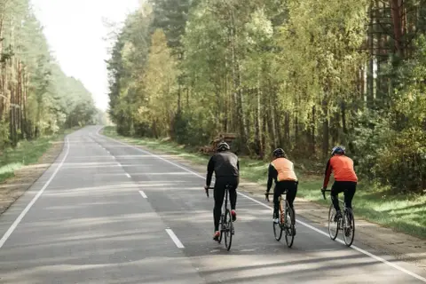 Trzech rowerzystów jedzie obok siebie leśną drogą. Czy można jechać rowerem obok siebie? Tak, jeśli droga jest wystarczająco szeroka i bezpieczna.