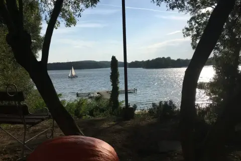 Sielankowy widok na jezioro w Sierakowskim Parku Krajobrazowym. Żaglówka sunie po falach, a na brzegu czeka ławka i dynia.