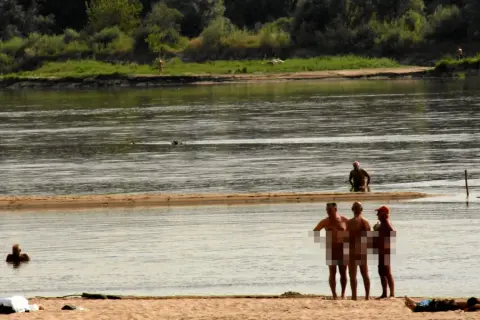 Ludzie opalają się i kąpią na piaszczystej plaży nad rzeką. To popularne miejsce, gdzie można spotkać plażę nudystów.