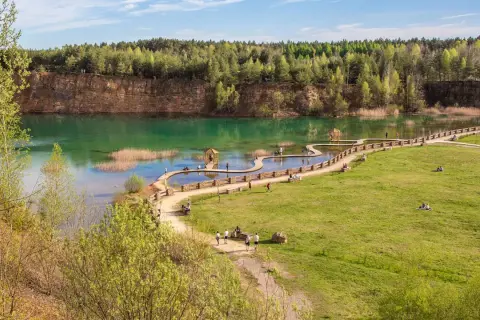 Malowniczy park Gródek Jaworzno z turkusową wodą, drewnianymi kładkami i zielonymi terenami rekreacyjnymi.