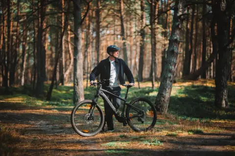 Mężczyzna z rowerem w lesie, gotowy do odkrywania tras rowerowych Łeba.