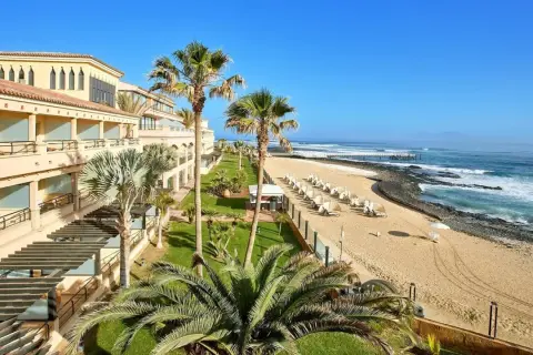 Hotel z widokiem na plażę i ocean. Palmy, leżaki i spokojne morze. Idealne miejsce na Fuerteventurze, gdzie najmniej wieje.