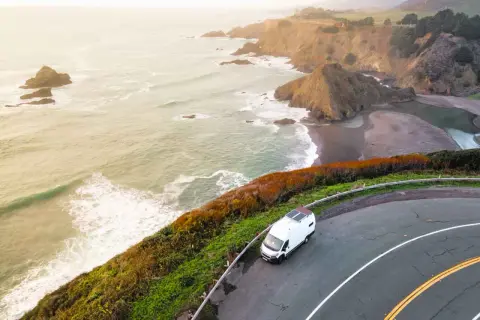 Biały kamper na krętej drodze wzdłuż wybrzeża Pacyfiku, idealny na road trip USA. Fale rozbijają się o skaliste klify.