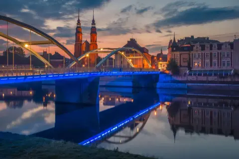 Zachód słońca nad Odrą, most z niebieskim podświetleniem i katedra w tle. Odkryj magiczne miejsca opolskie.